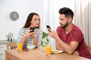 Obraz na płótnie Canvas Distrustful young woman peering into boyfriend's smartphone at home