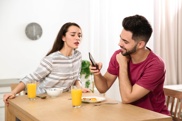Distrustful young woman peering into boyfriend's smartphone at home