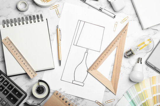 Flat lay composition with drawing of lamp on white marble table. Designer's workplace