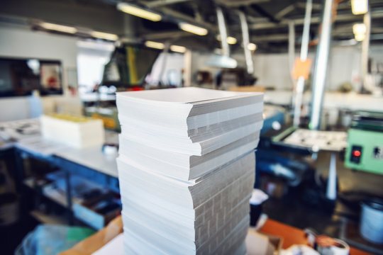 Picture of printing shop interior. Selective focus on pile of sheets.