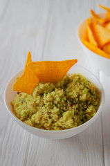 Nachos and guacamole on a white wooden table.