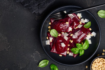 Beetroot ravioli with goat cheese, basil and pine nuts in a black plate against a dark background.  Ravioli inside with a filling of baked beets. Vegetarian food.  Space for text. Top view