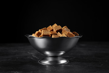 Metal bowl with brown sugar cubes on black table