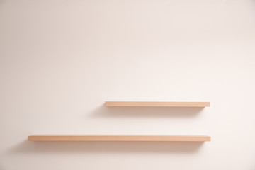 Empty stylish wooden shelves on light wall