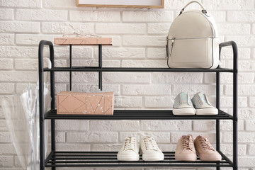 Fototapeta na wymiar Shelving rack with stylish women's shoes and accessories near white brick wall indoors
