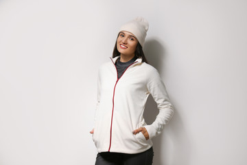 Woman wearing fleece jacket and hat on light grey background. Winter sport clothes