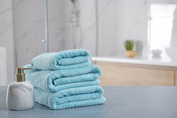 Stack of clean towels and soap dispenser on grey stone table in bathroom. Space for text