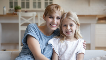 Portrait of smiling mum and little daughter relax on couch