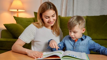 Beautiful mother and son studying together at home. Home education concept. Nanny teaching a boy at home doing homework.