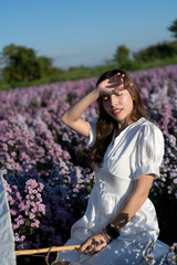 Woman in white dress with white umbrella posing in purple margaret flower field.