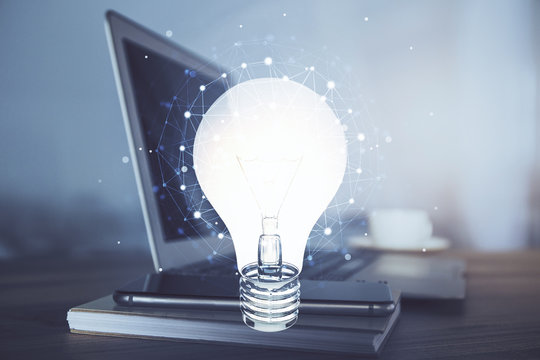 Computer on desktop in office with bulb icon hologram. Multi exposure. Concept of idea.