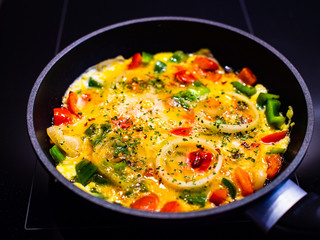 Preparing breakfast - scrambled eggs with vegetables on black stone background