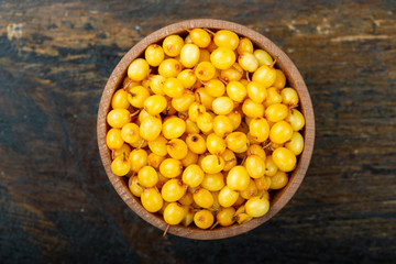 Ripe sea-buckthorn berries in a wooden bowl on the table.
