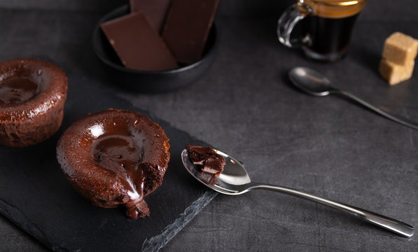 Warm chocolate lava cake on a black plate with a cup of coffee on a dark background