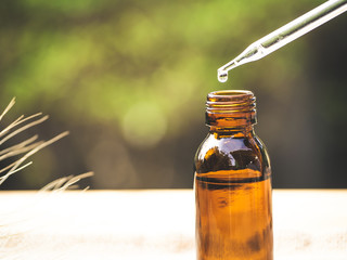 The essential oil falling from glass dropper into organic bio alternative medicine, brown bottle.