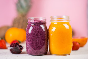 Two jars of multi-colored smoothie on a pink background.