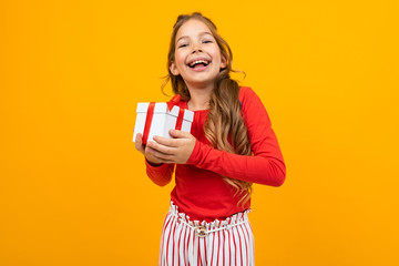 joyful smiling young girl with a gift box on a yellow background with copy space
