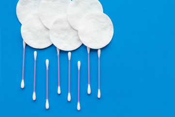 Cotton pads and cotton sticks in the form of clouds and rain on a blue background with a place for...