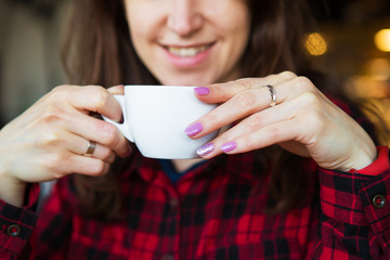 The girl smiles while holding a cup of coffee. Close-up.