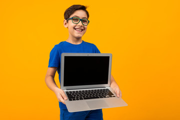caucasian boy holds laptop screen forward with mock up on yellow studio background with copy space
