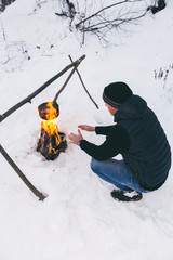 Man is preparing a fire and boiling water for cooking, winter camping.