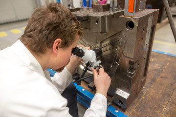 Quality engineer checks deficiencies on the injection mold by a microscope, industrial concept