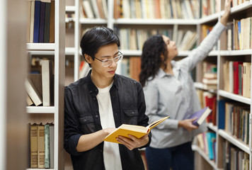 Focused japanese guy reading book at library