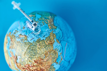 Medical syringe and ampoule with a medicine against Earth globe. Virus threat and epidemic...