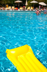Bright yellow lilo floating in the sun on a rippling blue swimming pool