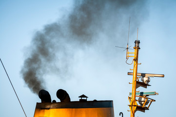Close up of the polluting soot exhaust of the smokestack of a Turkish ferry against blue sky in...