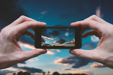 Hands Holding Mobile Phone - Camera and Taking Picture of Moon on Dark Sky with Clouds