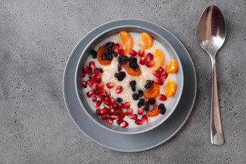 gray plate of oatmeal with pomegranate seeds, tangerine slices, raisins, dried apricots on a gray background