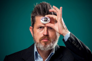 A portrait of man in suit holding egg with drawing eye near fore