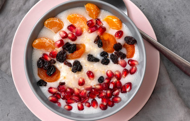 plate of oatmeal with Mandarin slices, pomegranate seeds, raisins, dried apricots, porridge with a spoon