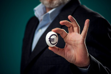 A portrait of man in suit holding white egg with drawing dollar sign. Business and finance concept