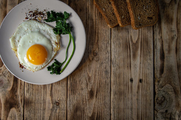 Eggs with seasonings and greens on a white plate with rye bread on a wooden table
