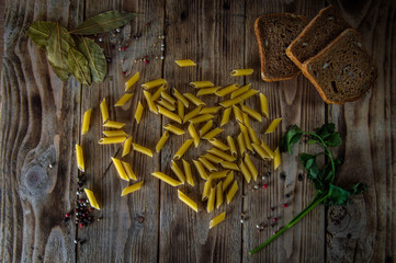 Pasta lie on a wooden table along with bread herbs, and seasonings