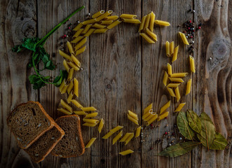 Pasta lie on a wooden table along with bread herbs, and seasonings