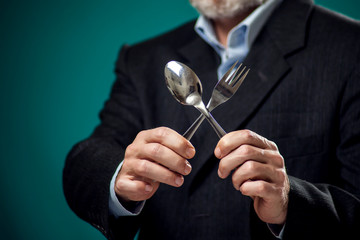 A portrait of hungry man in suit holding spoon and fork.