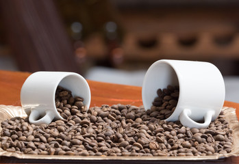 Close view of two white cups on their sides with coffee beans spilling out of it onto a tray of...