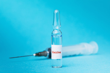 Transparent ampoule with a virus vaccine and a syringe on a blue background