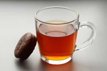 Glass transparent Cup with black tea and delicious chocolate dessert next to it on a gray background. Selective focus.