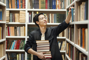 Young chinese man in glasses picking book at library