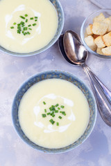 Potato leek soup in blue ceramic bowl garnished with french cream and green onion, served with croutons, vertical, top view
