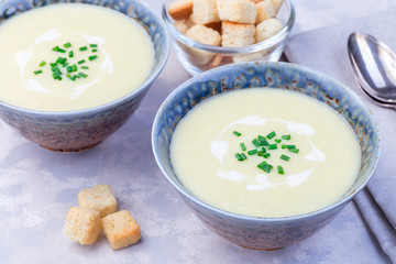 Potato leek soup in blue ceramic bowl garnished with french cream and green onion, served with croutons, horizontal