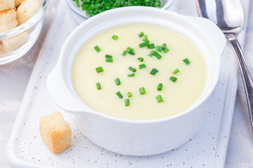 Potato leek soup in white ceramic bowl garnished with green onion served with croutons, horizontal, closeup