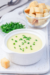 Potato leek soup in white ceramic bowl garnished with green onion served with croutons, vertical