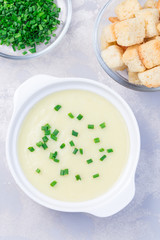Potato leek soup in white ceramic bowl garnished with green onion served with croutons, vertical, top view, closeup