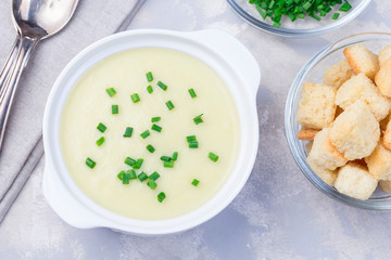 Potato leek soup in  white ceramic bowl garnished with green onion served with croutons, horizontal, top view