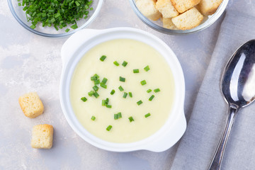 Potato leek soup in a white ceramic bowl garnished with green onion served with croutons, horizontal, top view